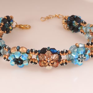 May include: A beaded bracelet with a gold, black and blue colour scheme. The bracelet features a repeating pattern of flower-shaped beads.