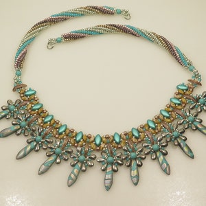 Peut inclure: Un collier de perles turquoise et or avec un motif g&eacute;om&eacute;trique. Le collier pr&eacute;sente une rang&eacute;e centrale de perles avec deux rang&eacute;es de perles plus petites de chaque c&ocirc;t&eacute;. Le collier est accentu&eacute; par des perles en forme de fleur turquoise et argent et de longues perles turquoise pointues.