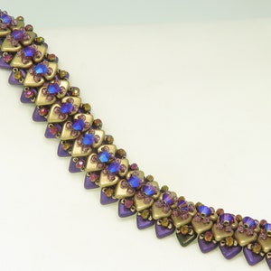 May include: A purple and gold beaded bracelet with a geometric pattern. The bracelet is made with small, faceted beads in a variety of shapes and sizes.