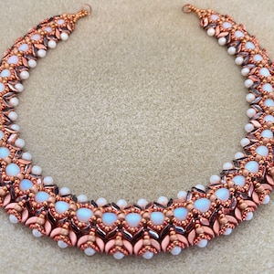 Peut inclure: Un collier de perles en cuivre et blanc avec un motif géométrique. Le collier est composé de petites perles rondes et de perles ovales plus grandes.