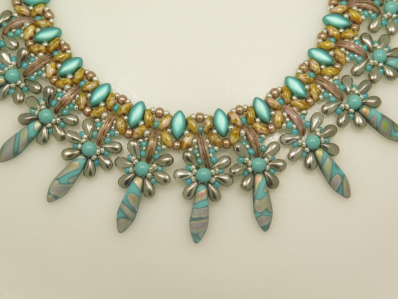 Peut inclure: Un collier de perles turquoise et argent avec un motif floral. Le collier a un design multi-brins avec une rang&eacute;e de perles turquoise et argent en bas.