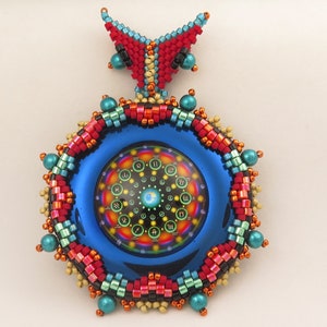 May include: A beaded pendant with a blue, round, mirrored surface featuring a colourful, circular design with numbers and symbols. The pendant is surrounded by a beaded border with red, orange, yellow, green, and blue beads.