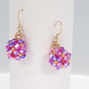 Puede incluir: Un par de pendientes de oro con racimos de flores de cristal iridiscente rosa y morado.