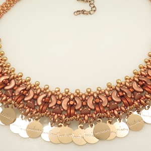 Könnte beinhalten: Eine goldene und kupferfarbene Perlenkette mit geometrischem Muster und goldenen Münzenanhängern, auf denen "handgefertigt" steht.