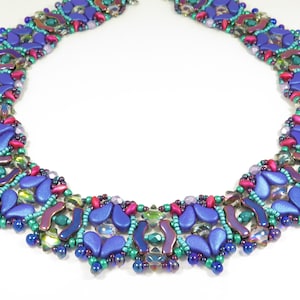 May include: A beaded necklace featuring a geometric design in shades of blue, green, and purple. The necklace is crafted with a variety of bead sizes and shapes, including teardrop, round, and rectangular beads.