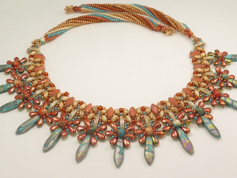 Peut inclure: Un collier multi-rangs de perles avec un motif g&eacute;om&eacute;trique. Le collier pr&eacute;sente une vari&eacute;t&eacute; de perles dans des tons de brun, orange et turquoise. Les perles sont dispos&eacute;es en un motif de fleurs et de pointes.