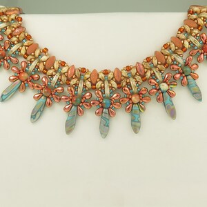 Peut inclure: Un collier de perles avec un design multi-brins pr&eacute;sentant un motif floral r&eacute;p&eacute;titif. Le collier est compos&eacute; d'un m&eacute;lange de perles brun clair, orange et bleues.