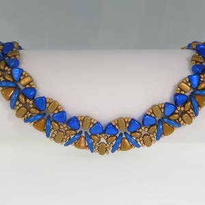 Op de afbeelding: Een blauwe en gouden kralen armband met een geometrisch patroon. De armband is gemaakt met kleine, ronde kralen en driehoekige kralen.