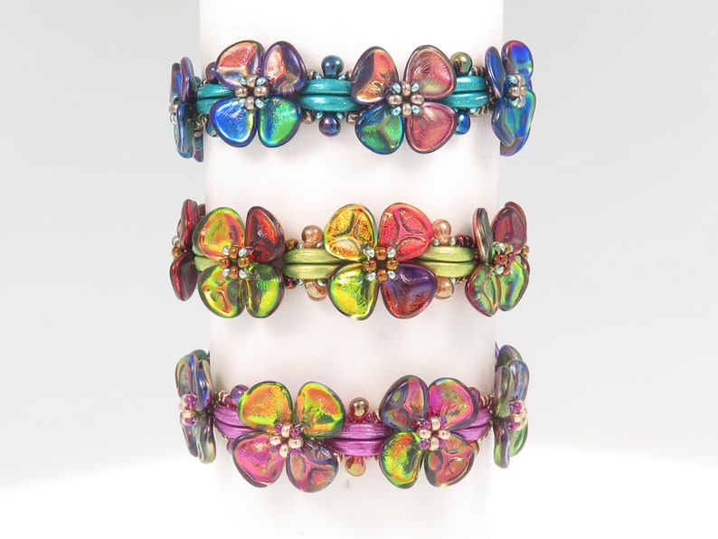 Peut inclure: Trois bracelets de perles orn&eacute;s de perles en verre iris&eacute; en forme de fleurs. Le bracelet du haut a des entretoises bleu sarcelle, celui du milieu des entretoises vert citron et celui du bas des entretoises magenta. Chaque bracelet est fait de petites perles m&eacute;talliques.
