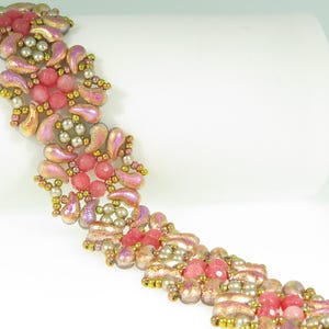 May include: A beaded bracelet with a repeating pattern of pink, gold, and iridescent beads. The bracelet includes round pink beads, small gold beads, and larger, teardrop-shaped iridescent beads. The design is intricate and detailed.