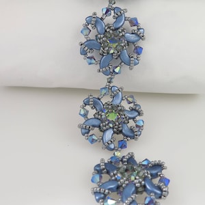 Könnte beinhalten: Ein blaues Perlenarmband mit einem silbernen Verschluss. Das Armband besteht aus kleinen, runden Perlen und zeigt ein sich wiederholendes Muster aus Blumenformen.