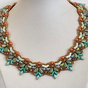 Może przedstawiać: Naszyjnik z koralików w kolorze miedzianym, zielonym i białym. Naszyjnik wykonany jest z małych, fasetowanych koralików ułożonych w geometryczny wzór.