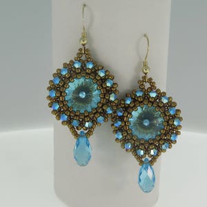 May include: A pair of dangle earrings with a blue crystal centre surrounded by gold beads. The earrings have a teardrop-shaped blue crystal dangling from the bottom.