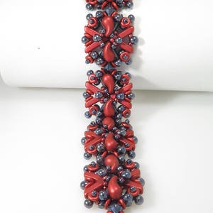 May include: A red and dark grey beaded bracelet with a geometric design. The bracelet is made of small, round beads and has a magnetic clasp.