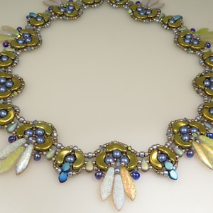 Può includere: Una collana artigianale con un design floreale. Presenta elementi in metallo dorato, accenti iridescenti a forma di foglia e perline blu e color perla. La collana è progettata con un motivo delicato e intricato.