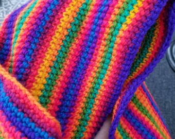 May include: A colorful crocheted scarf with stripes of red, orange, yellow, green, blue, purple, and pink.