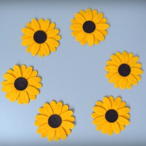 Pode incluir: Seis girassóis de feltro amarelo com centros pretos dispostos em círculo sobre um fundo azul claro.