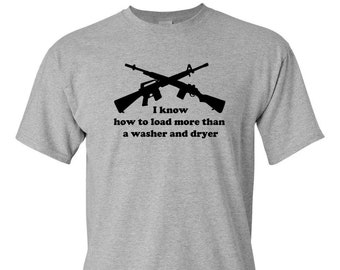 May include: A light gray t-shirt featuring a black graphic of two crossed rifles. Below the rifles is the text: "I know how to load more than a washer and dryer."