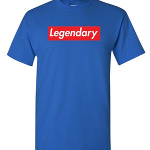 May include: Royal blue t-shirt with the word "Legendary" in white text inside a red rectangular box on the front. The shirt has short sleeves and a crew neck.