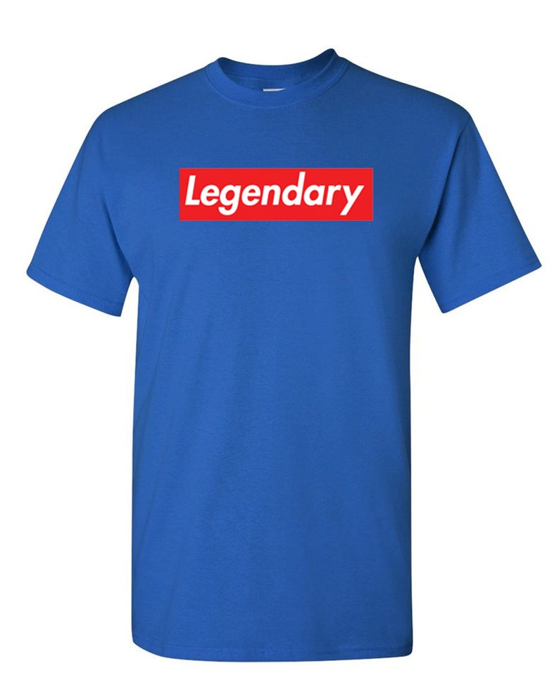 May include: Royal blue t-shirt with the word "Legendary" in white text inside a red rectangular box on the front. The shirt has short sleeves and a crew neck.