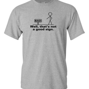 May include: A gray t-shirt with a stick figure illustration and the text "Well, that's not a good sign." The stick figure is standing in front of a sign that says "BAD".
