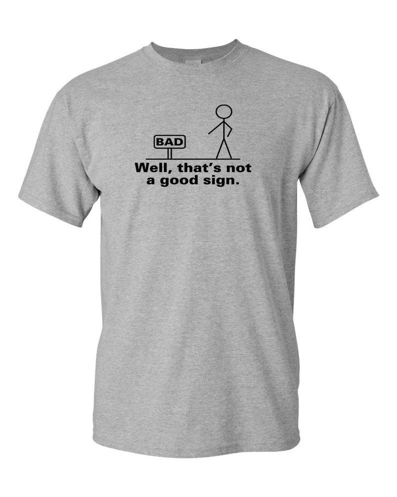 May include: A gray t-shirt with a stick figure illustration and the text "Well, that's not a good sign." The stick figure is standing in front of a sign that says "BAD".