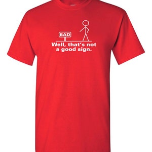 May include: Red t-shirt with a white stick figure standing in front of a sign that says "BAD". The text below the figure says "Well, that's not a good sign."