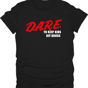 Puede incluir: Camiseta negra con el texto rojo "D.A.R.E. TO KEEP KIDS OFF DRUGS". El texto es en negrita y con un efecto desgastado. La camiseta es de cuello redondo.