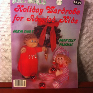 May include: A magazine cover for Doll World issue #3, featuring a holiday wardrobe for adopted kids. The cover features two dolls wearing red and white pajamas and a red nightshirt. The dolls are holding red ornaments and there is a red and green Christmas wreath in the background. The text on the cover reads "Holiday Wardrobe for Adopted Kids" and "Dorm Shirt" and "Drop Seat Pajamas".