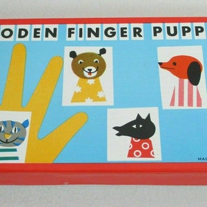 May include: A red box with the words "WOODEN FINGER PUPPETS" printed on the front. The box contains five finger puppets: a cat, a dog, a bear, a wolf, and a donkey. The puppets are made of wood and are painted in bright colors. The box is made in Czechoslovakia.