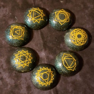 May include: Seven round, dark green, glittery stones with gold chakra symbols. Each stone represents a different chakra.