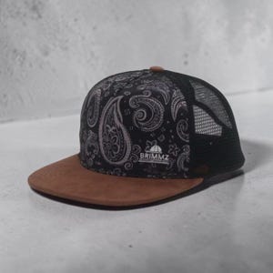 May include: A black and brown trucker hat with a paisley pattern on the front panel and a brown brim. The hat has a black mesh back and the text "BRIMMZ" is visible on the front.