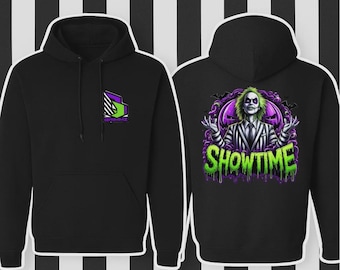 Puede incluir: Sudadera con capucha negra con bolsillo delantero y capucha. La parte delantera presenta un diseño geométrico en morado, verde y blanco. La parte trasera muestra un gráfico colorido de un personaje con la palabra "SHOWTIME" en letras verdes goteando.