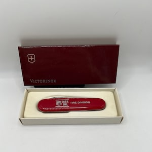 May include: A red Victorinox Swiss Army Knife with a white "MFA Oil Tire Division" logo on the handle. The knife is in its original box.
