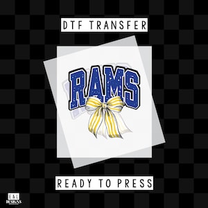 May include: DTF transfer design featuring the word "RAMS" in blue with a white outline, and a yellow and white bow. The words "DTF TRANSFER" and "READY TO PRESS" are printed above and below the design, respectively. The background is a black and white checkered pattern.