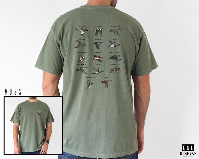 May include: Moss green t-shirt featuring a detailed illustration of various duck species in flight. The back of the shirt displays a grid of colorful duck illustrations with their names. The shirt is a comfortable, casual style.
