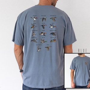 May include: Blue jean-colored t-shirt featuring a detailed illustration of various duck species in flight. The shirt has a classic crew neck and short sleeves. The text "BLUE JEAN" is printed on the bottom right corner of the image.