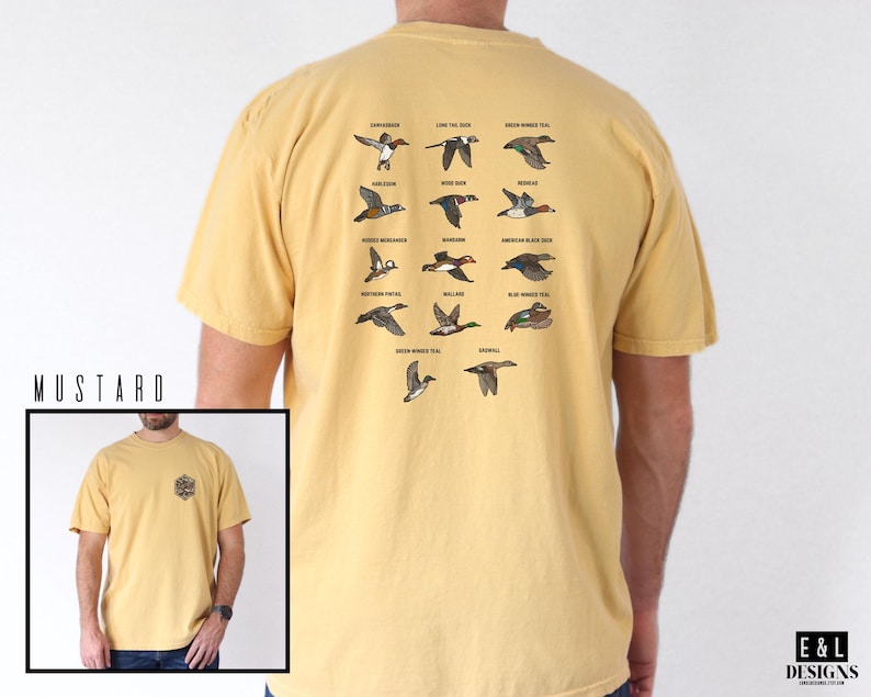 May include: Mustard-colored t-shirt featuring a detailed graphic of various duck species with their names. The shirt has a small graphic on the front and the text "E & L DESIGNS" on the bottom right.