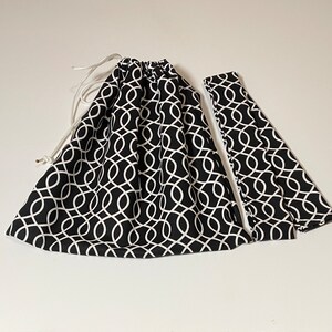 May include: A black and white drawstring bag with a geometric pattern. The bag is made of fabric and has a white drawstring.