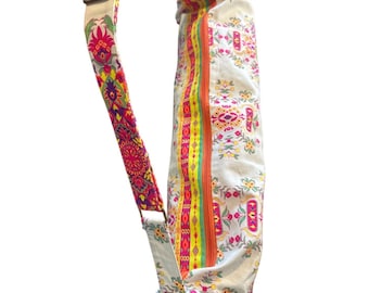 May include: A cylindrical yoga mat bag featuring a white base with a colorful floral pattern in shades of pink, yellow, orange, and green. It includes a long, adjustable shoulder strap with a matching vibrant floral print and a zipper.