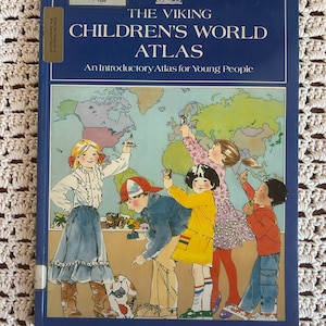 May include: A vintage copy of "The Viking Children's World Atlas" with a blue cover. The cover features illustrations of children pointing at a world map. The title and author's name are printed in white. The book is an introductory atlas for young people.