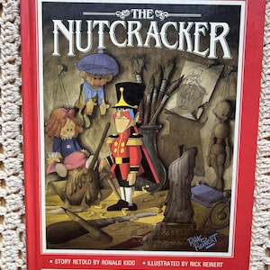 May include: A hardcover book titled "The Nutcracker" with a red cover. The cover features an illustration of the Nutcracker character in a red and gold uniform, surrounded by other characters and props. The author and illustrator's names are also on the cover.