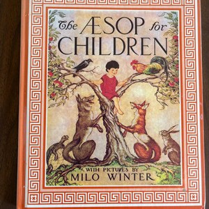May include: A hardcover book titled The Aesop for Children with pictures by Milo Winter. The cover features a central illustration of a child sitting in a tree surrounded by a crow, a rooster, a wolf, a fox, a turtle, and a rabbit.