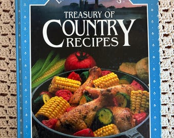 May include: A hardcover cookbook titled Land O Lakes Treasury of Country Recipes. The blue cover features a white floral pattern and a central image of a cast iron skillet filled with roasted chicken, corn on the cob, and vegetables.