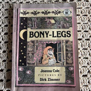May include: A paperback book titled Bony-Legs by Joanna Cole with illustrations by Dirk Zimmer. The cover features a witch in a window, a crescent moon, bats, and skull patterns. The Scholastic Hello Reader logo is visible in the top right corner.