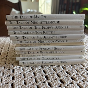 May include: A stack of twelve small hardcover books with white spines and black text. The titles include The Tale of Mr. Tod, The Tale of Mrs. Tittlemouse, The Tale of The Flopsy Bunnies, The Tale of Tom Kitten, The Tale of Mr. Jeremy Fisher, and others.