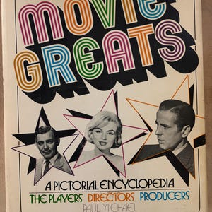 May include: A vintage book cover titled "Movie Greats" with colorful, retro lettering. The cover features portraits of classic Hollywood stars like Marilyn Monroe. The text reads "A Pictorial Encyclopedia" and lists "The Players, Directors, Producers."