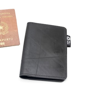 Puede incluir: Un portapasaporte negro hecho de cámaras de aire de neumáticos recicladas. El portapasaporte tiene una pequeña etiqueta con el texto "Pelz Aveia" en el lado derecho.
