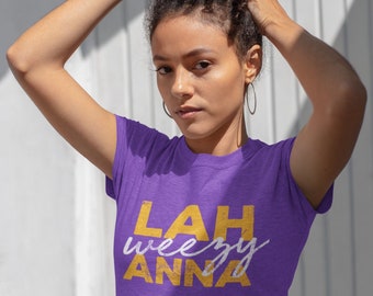 Puede incluir: Camiseta morada con el texto "LAH weezy ANNA" en letras amarillas.