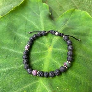 May include: A black lava rock bracelet with three green and pink gemstone beads and silver accents.
